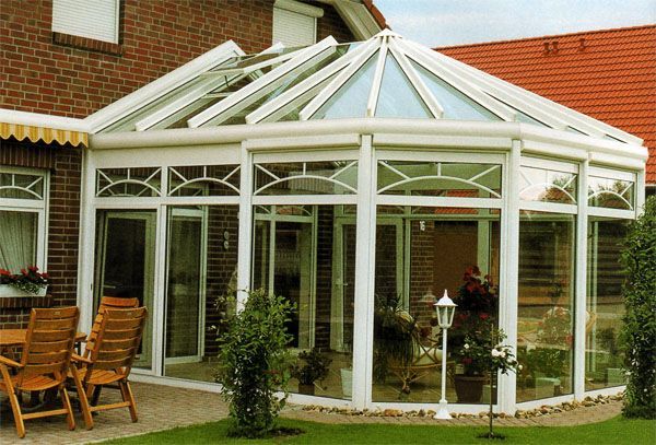 Halbrunder Wintergarten mit weißer Konstruktion und großen Fenstern, der viel Licht hereinlässt