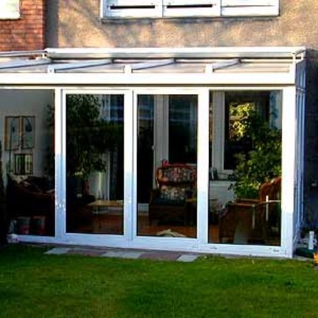 Wintergarten mit weißem Gestell, davor Rasenfläche